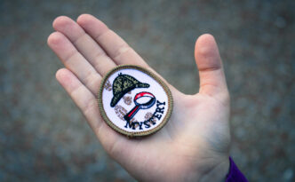 Child's hand holding a scouting patch that says "Mystery"